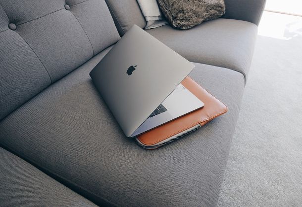Imagen de un ordenador portátil Apple parcialmente cerrado, colocado sobre una funda de piel marrón sobre un sofá gris. El entorno sugiere comodidad, espacio de trabajo híbrido o sesión online. Esta imagen representa el enfoque flexible y personalizado del servicio de orientación laboral ofrecido por Raquel Egido, psicóloga profesional, dirigido a personas que desean definir nuevos objetivos profesionales, gestionar transiciones laborales o mejorar su bienestar psicológico en el ámbito del trabajo. Refuerza la idea de acompañamiento emocional en contextos de desarrollo profesional y toma de decisiones.